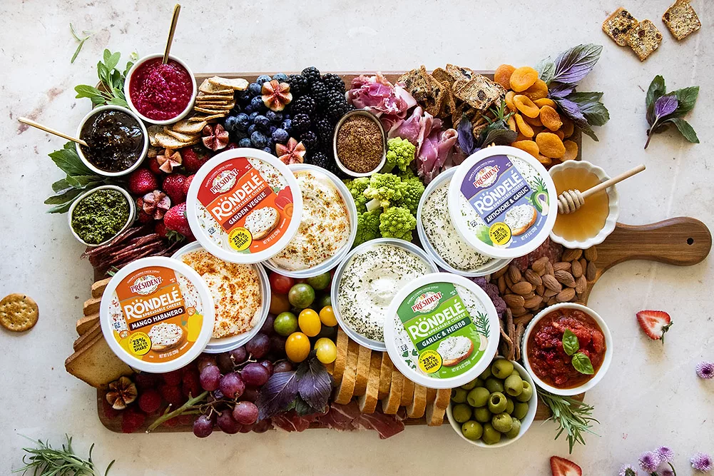A table spread with froits and tubs of spreadable chees on top